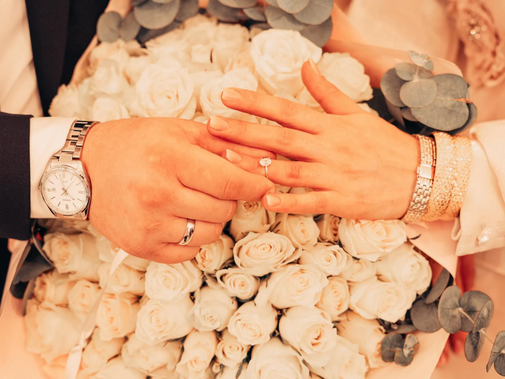 Cặp đôi nắm tay đeo nhẫn cưới vàng hồng, biểu tượng của tình yêu vĩnh cửu và lãng mạn